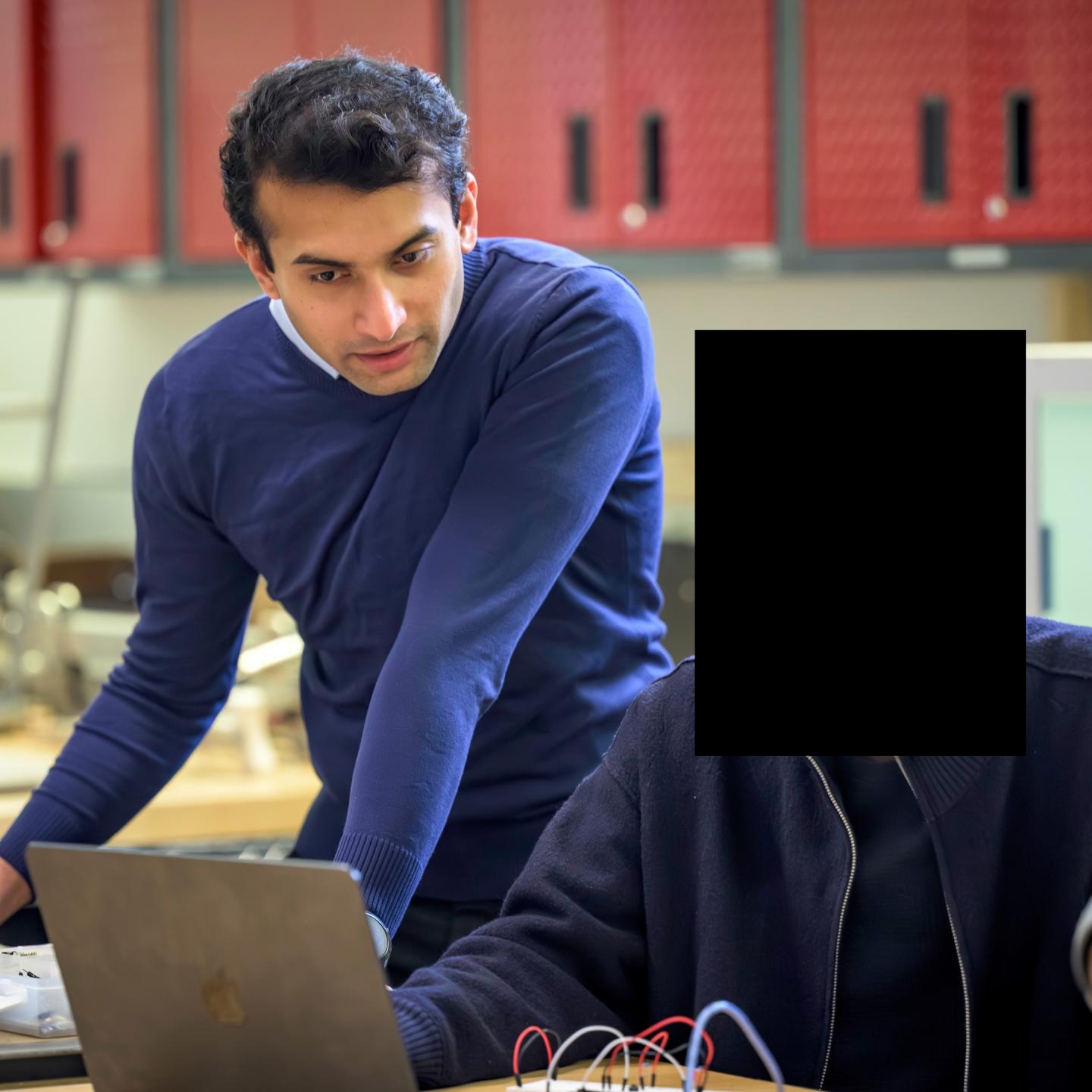 Shreyas leaning over a laptop while helping with a computing project